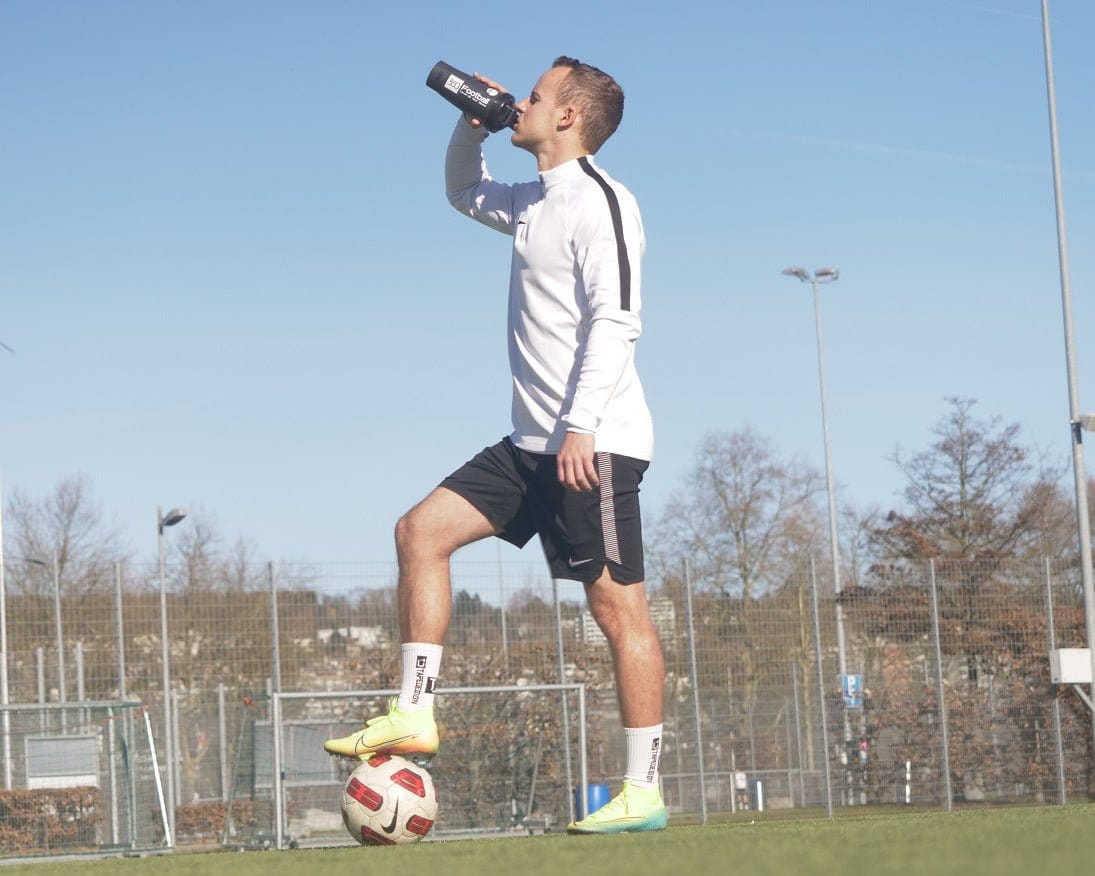 Nic von 360Football trinkt aus einem 360Football Shaker und steht auf einem Fussballplatz