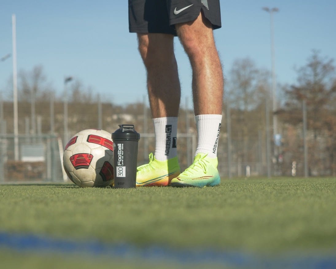 Der 360Football Shaker steht neben einem Fussballer und Ball auf einem Kunstrasen