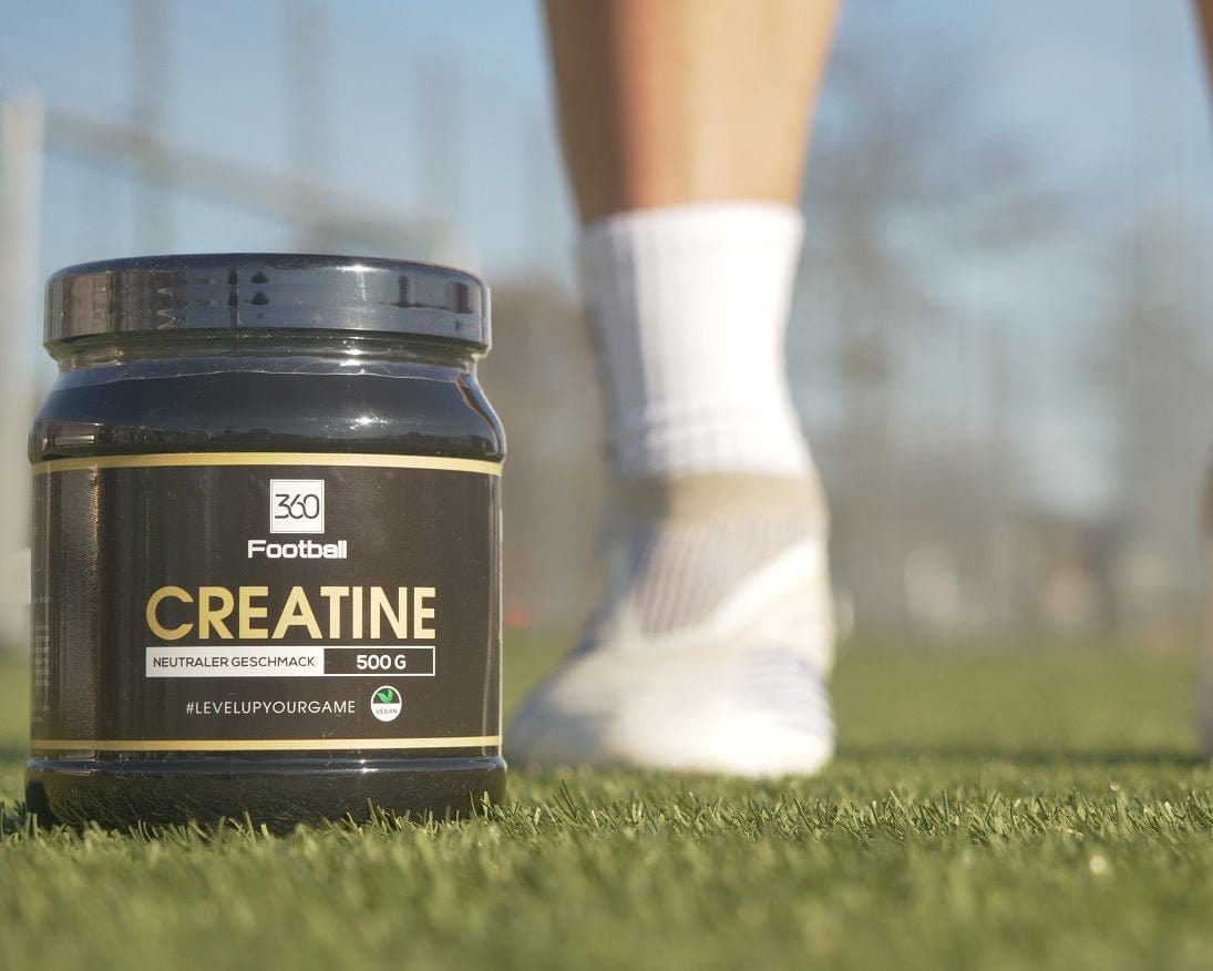 Das Creatine360 steht auf einem Fussballplatz, im Hintergrund sieht man einen Fussballer