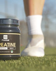 Das Creatine360 steht auf einem Fussballplatz, im Hintergrund sieht man einen Fussballer